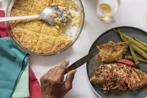 Assiette de plat antillais traditionnel avec poisson entier, légumes et gratin, sur une table dressée avec serviettes colorées