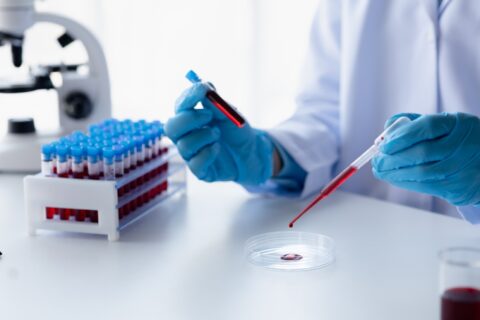 Scientifique manipulant un échantillon de sang en laboratoire, avec des tubes à essai, symbolisant les analyses biologiques.