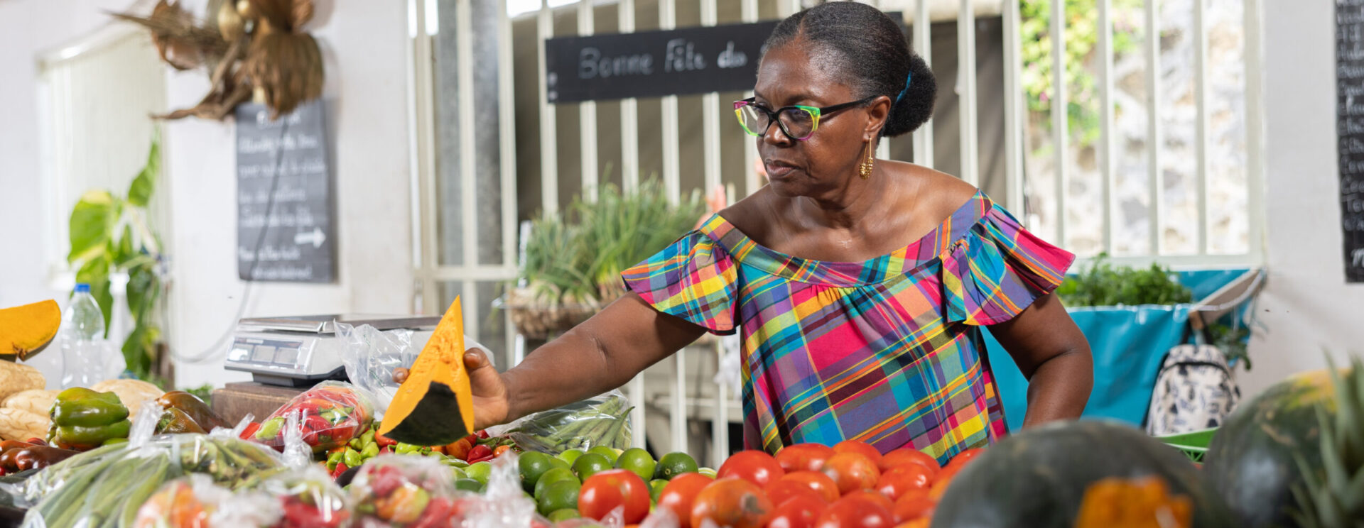 Vendeuse présentant un giraumon sur un étal de fruits et légumes dans un marché local aux Antilles.