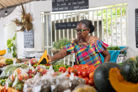 Vendeuse présentant un giraumon sur un étal de fruits et légumes dans un marché local aux Antilles.