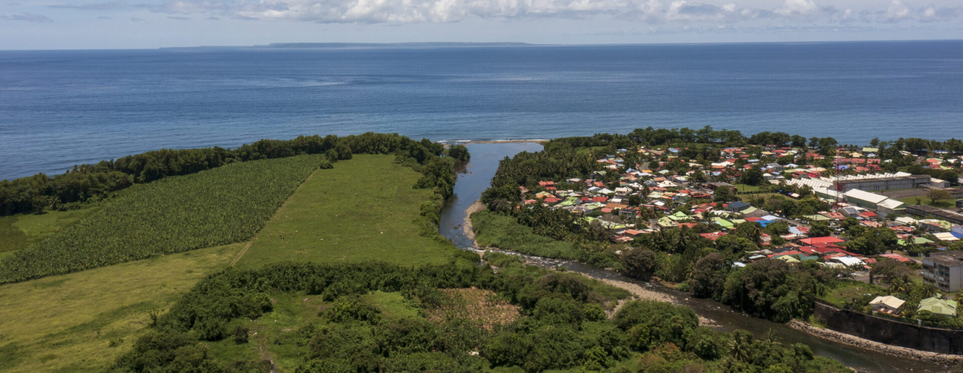 Vue aérienne d’un littoral antillais avec une rivière se jetant dans la mer, bordée de zones agricoles et d’habitations colorées