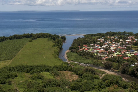Vue aérienne d’un littoral antillais avec une rivière se jetant dans la mer, bordée de zones agricoles et d’habitations colorées