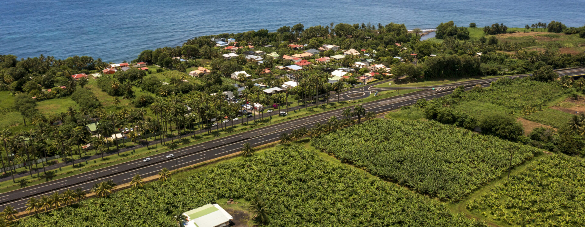 Vue aérienne d'une route littorale séparant des champs agricoles de la mer