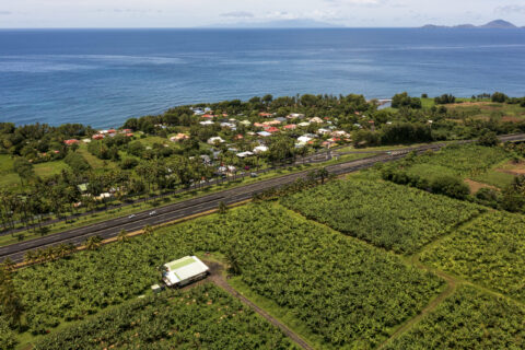 Vue aérienne d'une route littorale séparant des champs agricoles de la mer